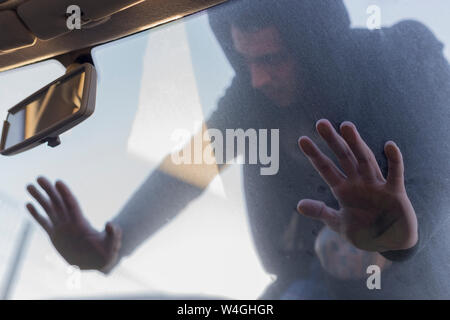 Young man leaning on windscreen of an old car on scrapyard Stock Photo