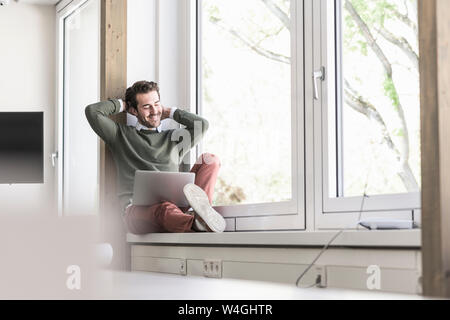 Young businessman sitting on windowsill, using laptop Stock Photo