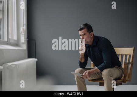 Mature businessman sitting on chair with tablet Stock Photo