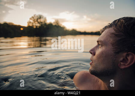 Young man swimming in lake, watching sunset Stock Photo