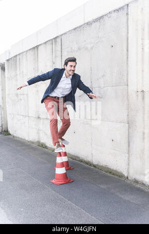 Young man balancing on traffic cones in front of concrete wall Stock Photo