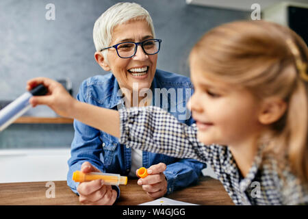 Grandmother and granddaughter sitting at table, painting colouring book Stock Photo