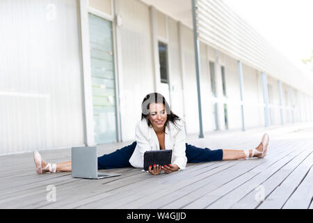Female balett dancer sitting on the ground, using tablet and laptop Stock Photo