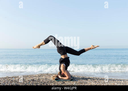Young woman practicing yoga on the beach, doing headstand Stock Photo