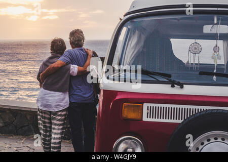 Senior couple traveling in a vintage van, looking at the sea with arms around Stock Photo