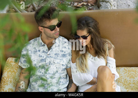 Relaxed young couple wearing sunglasses sitting outdoors Stock Photo