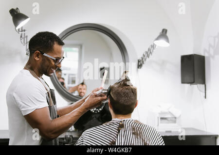 Smiling barber shaving and trimming hair of a customer in barber shop Stock Photo