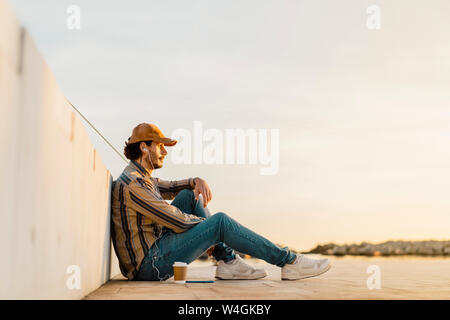 Man wearing baseball cap listening music with earphones and smartphone at sunset Stock Photo