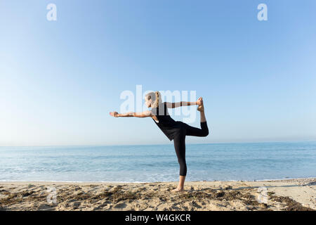 Young woman practicing yoga on the beach, doing dancer pose Stock Photo