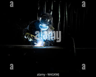 Industrial worker in protective clothing welding metal with welding torch Stock Photo