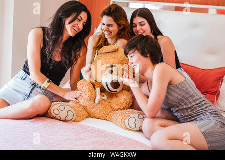 Girlfriends celebrating birthday, sitting with teddy bear on bed Stock Photo