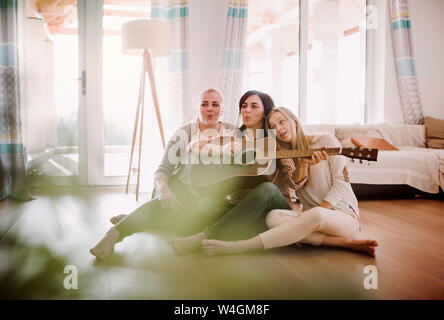 Mature woman with two daughters sitting on the floor playing guitar at home Stock Photo