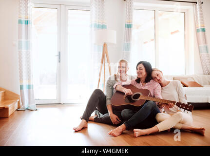 Mature woman with two daughters sitting on the floor playing guitar at home Stock Photo