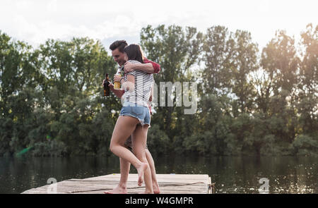 Happy young couple having a drink and embracing on jetty at a remote lake Stock Photo