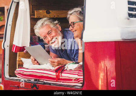Senior couple traveling in a vintage van, lying in boot, using digital tablet Stock Photo