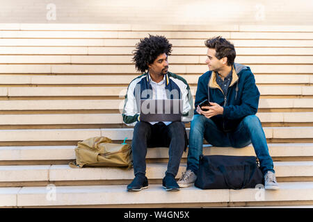 Two casual businessmen sitting on stairs working on laptop Stock Photo