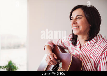 Portrait of smiling mature woman playing guitar at home Stock Photo