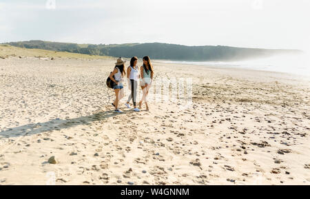 Three women with guitar walking on the beach Stock Photo