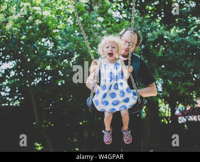 Father pulling swing with girl at playground Stock Photo