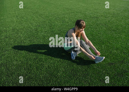 Sportswoman sitting on lawn and tying shoes Stock Photo