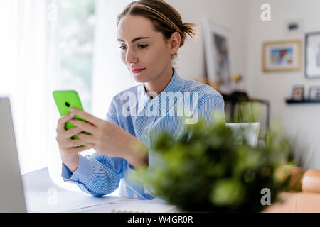 Woman in office using cell phone at table Stock Photo