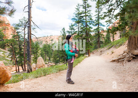 Woman carrying her daughter in a baby carrier at hoodoos in Bryce Canyon, Utah, USA Stock Photo