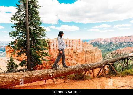 Traveler woman walking on the trunk of a fallen tree enjoying the view in Bryce Canyon, Utah, USA Stock Photo