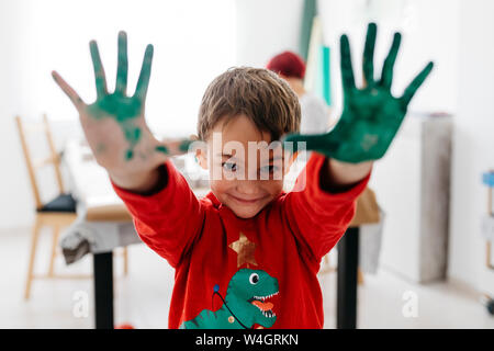 Boy showing his hands painted green while doing crafts at home Stock Photo