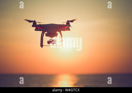 Silhouette of drone hovering in  beautiful sunset on the ocean. Stock Photo
