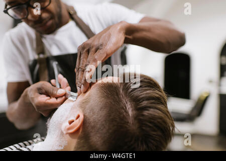 Man getting his beard shaved with razor in barber shop Stock Photo