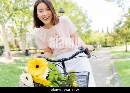 Portrait of happy young woman with flowers and bicycle in park Stock Photo