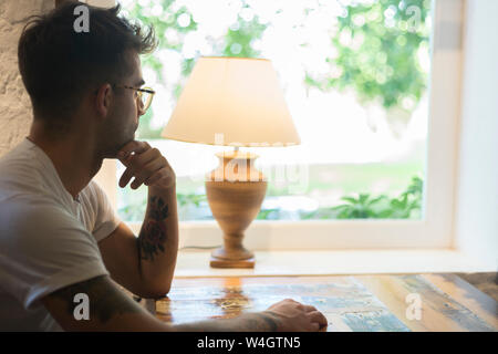 Young man sitting at table in a restaurant looking out of window Stock Photo