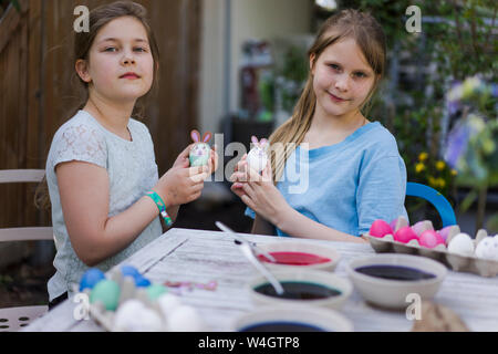 Portrait of two girls decorating Easter eggs on garden table Stock Photo