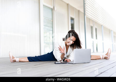 Female balett dancer sitting on the ground, using tablet and laptop Stock Photo