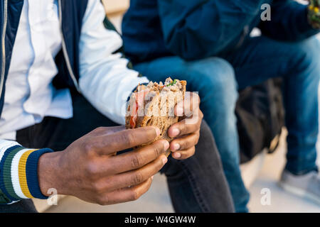 Close-up of two men sitting on stairs having lunch break Stock Photo