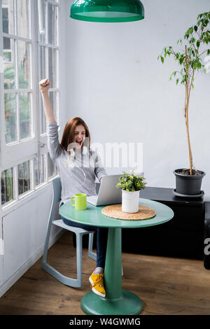 Excited young woman stting at table at home with laptop Stock Photo