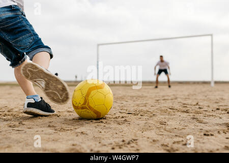 Close-up of man and boy playing soccer on the beach