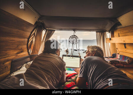 Senior couple traveling in a vintage van, using laptop Stock Photo