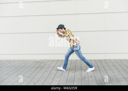 Young man wearing flat hat and aloa shirt, walking against headwind Stock Photo