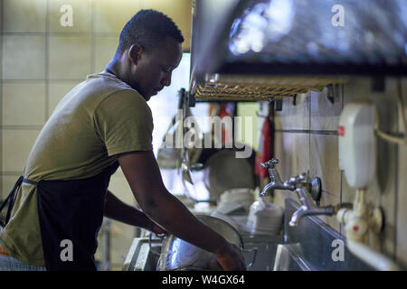 Young man washing dishes in restaurant kitchen, South Africa Stock Photo