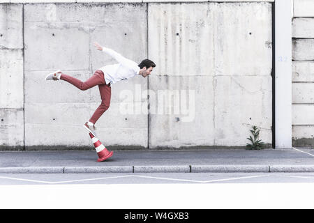 Young man balancing on traffic cone in front of concrete wall Stock Photo