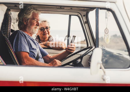 Senior couple traveling in a vintage van, using smartphone Stock Photo