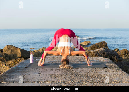 Young woman practicing yoga on the beach, doing prasarita padottanasana Stock Photo