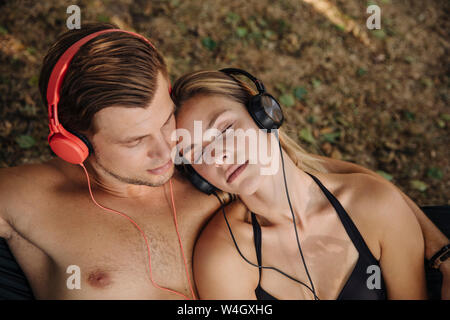 Young couple lying on grass, listening music with headphones Stock Photo