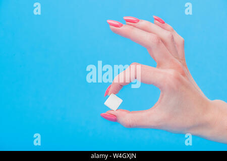cropped view of woman holding white sugar cube isolated on blue Stock Photo