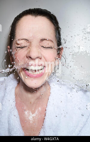 Water splashing into face of happy woman in bathrobe Stock Photo