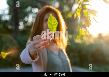 Young redheaded woman holding green leaf in a park Stock Photo