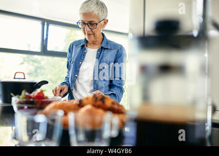 Senior woman standing in kitchen, chopping strawberries Stock Photo
