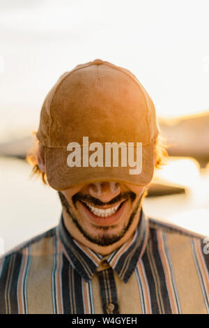 Laughing man wearing baseball cap at sunset Stock Photo