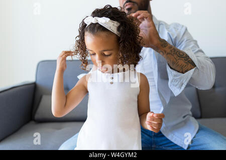 Father doing daughter's hair on couch at home Stock Photo